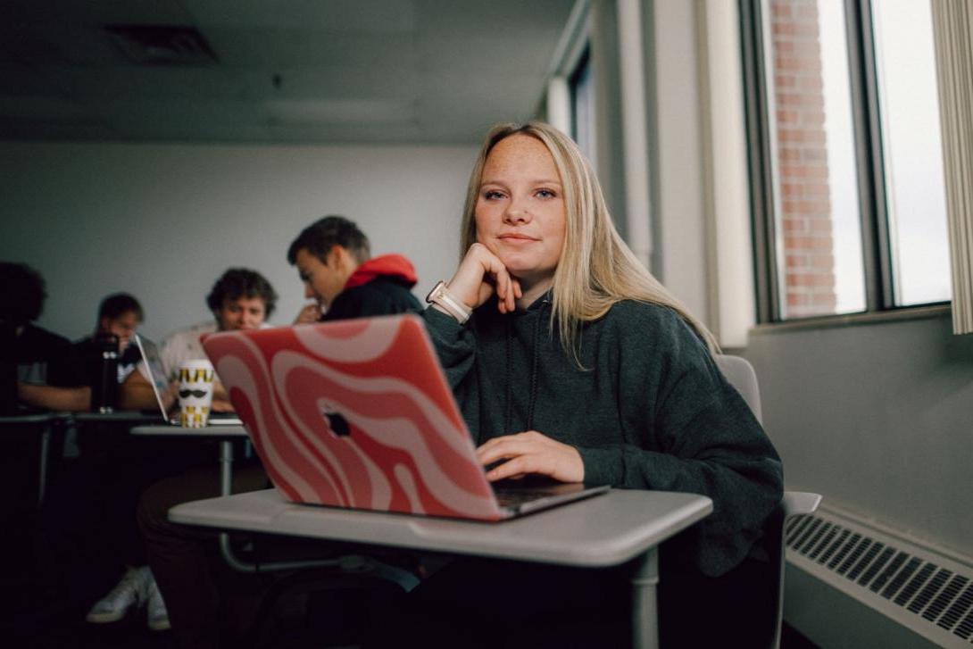 A Kettering management student sits in a classroom. On the desk is a laptop with a pink case.